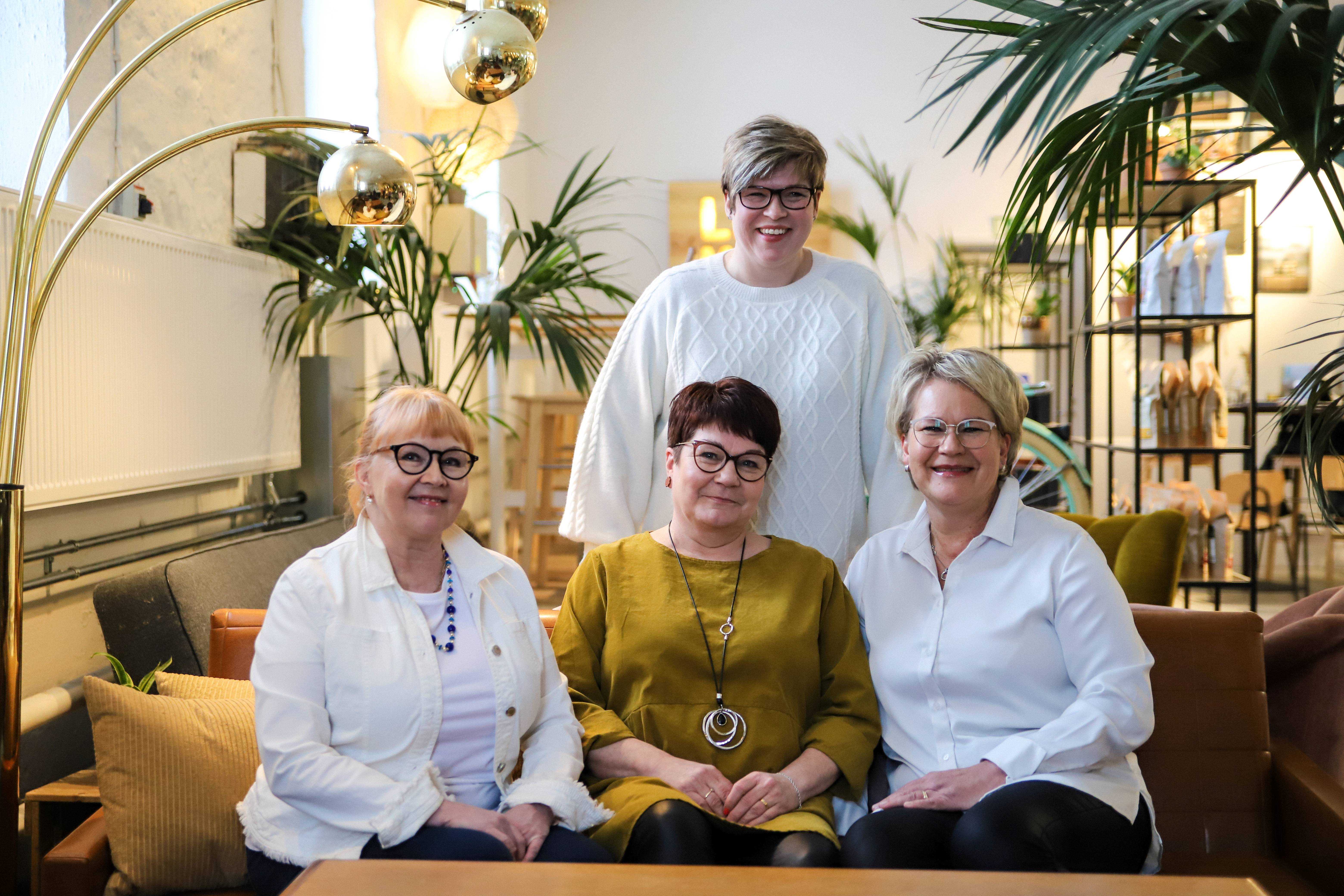 Neljä hymyilevää sairaanhoitajaa istuu kahvilassa sohvalla.